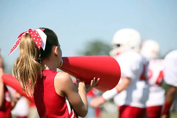 Cute Cheerleader supports her team by cheering through her Megaphone from the sidelines. Focus on Cheerleader.