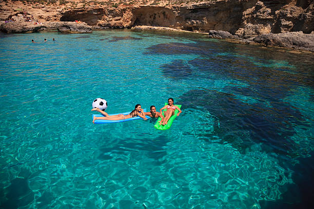 Group of friends enjoying their vacations. Swimming with inflatable soccer ball and lilo in beautiful blue lagoon.