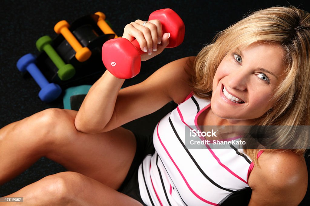Smiling Female does Fitness Workout Exercise and Weight Training Beautiful Female with fit body looking at camera lifting weights with dumbbells in background. 30-39 Years Stock Photo