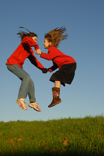 Children jumping together,and playing. Wearing red jumpers, hair flying, Playing on the grass with a clear blue sky in the background