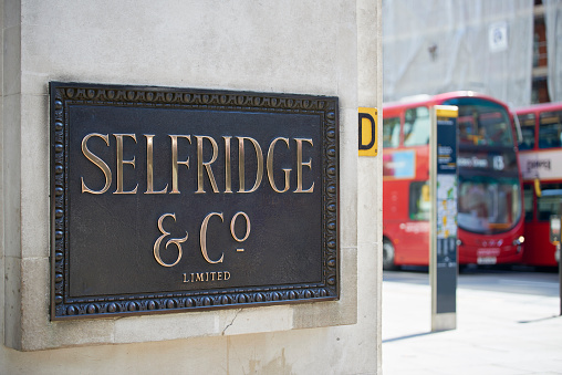 London, UK - April 22, 2015: Shop sign at the corner of famous department store Selfridge & Co., in Oxford Street, with red double-decker bus in the background.