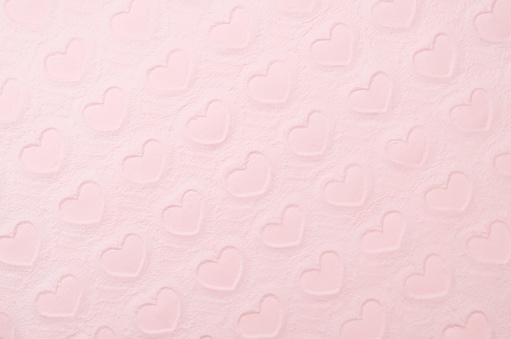 Abstract background of heart pattern hand-pressed into thick textured pink paper, shot at a tilt