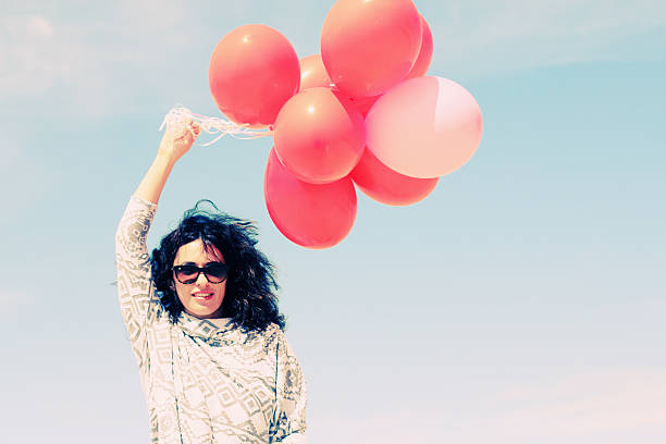 beautiful woman holding red balloons and walking on seaside