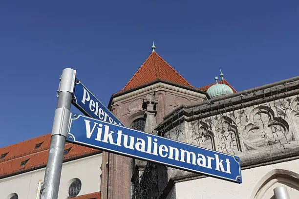 Munich Street Sign: Viktualienmarkt (The famous "Victuals Market" in the centre of Munich). In the Background the Church St. Peter, called Old Peter - the oldest parish church in Munich, Upper Bavaria, Bavaria, Germany. Selective Focus. Focus on the street sign.