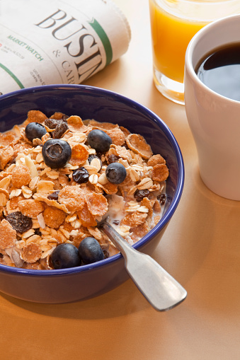 Bowl of cereal, blueberries, juice, coffee and newspaper for an early breakfast.