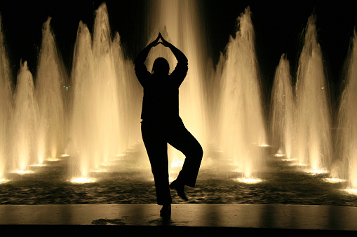 A woman strikes a distinctly Indian pose as she dances in front of a fountain.