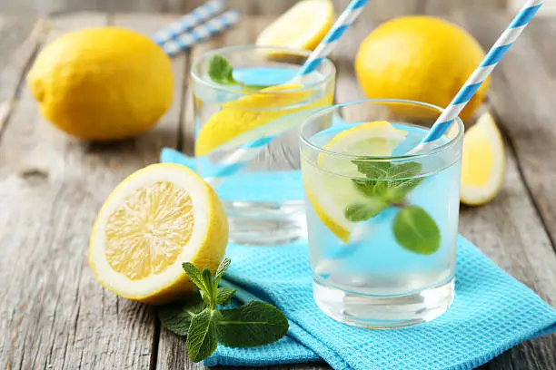 Fresh lemonade with lemon on grey wooden background