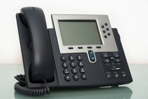 A modern business conference phone, with six phone lines - on a modern glass table, including reflection on the glass surface.