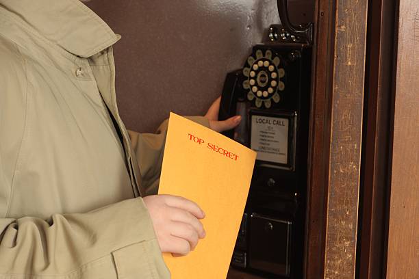 Cold War Spy - Top Secret Phone Call A cold-war era spy with an envelope marked "Top Secret" making a phone call from a phone booth. cold war photos stock pictures, royalty-free photos & images