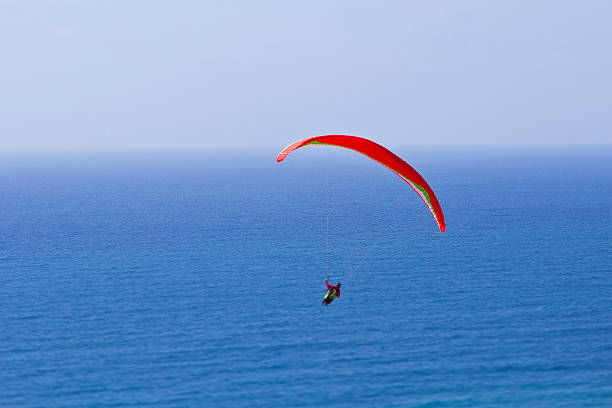 istock Paraglider with Orange Parachute with Blue Ocean and Sky Background 471145856