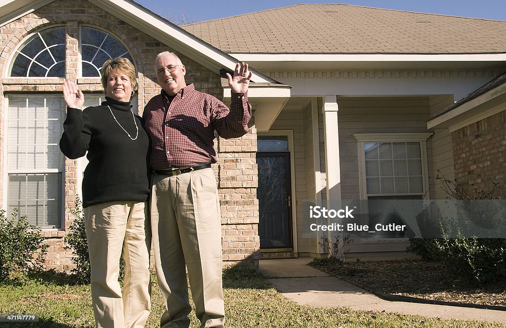 Senior Couple waving in front of house A Senior Couple in front of their house Happiness Stock Photo