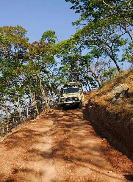 A safari fitted Landrover driving down a very steep dirt track in the African bush.