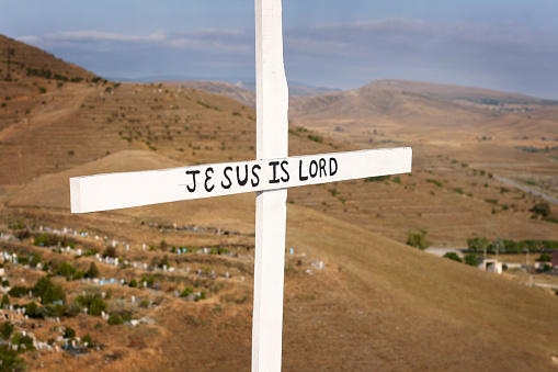 a wooden cross on a hill, overlooking a cemetery