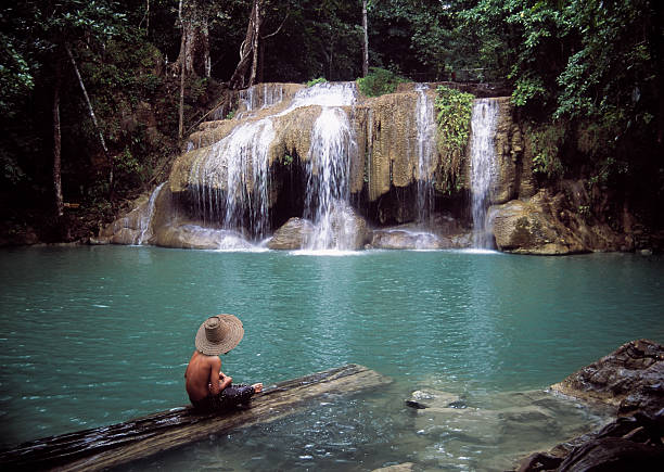앉은 젊은 남자 로그 옆에 태국의 폭포수형 - erawan falls 이미지 뉴스 사진 이미지