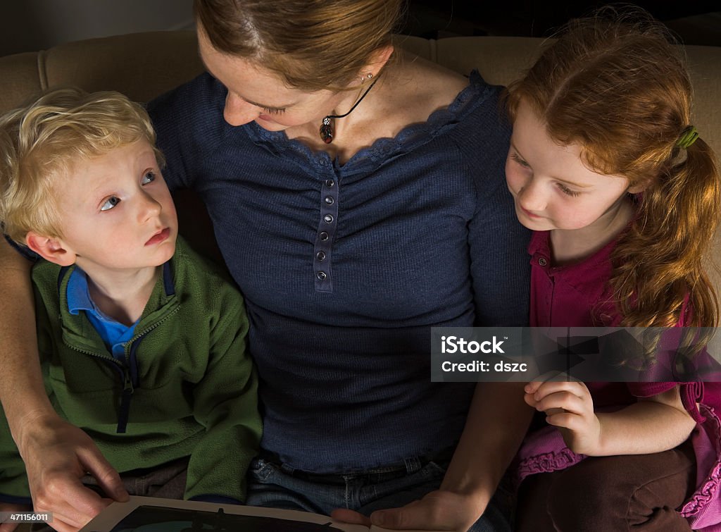 Jeune mère lire à son histoire de coucher deux petits enfants - Photo de Assistante maternelle libre de droits