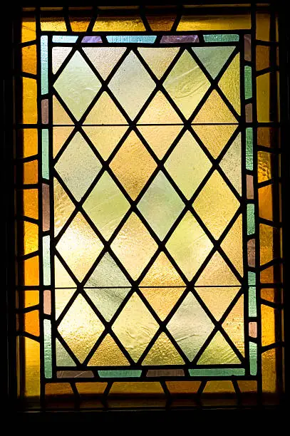 Soft light shines through an isolated stained glass window, dating to the early 1900's.