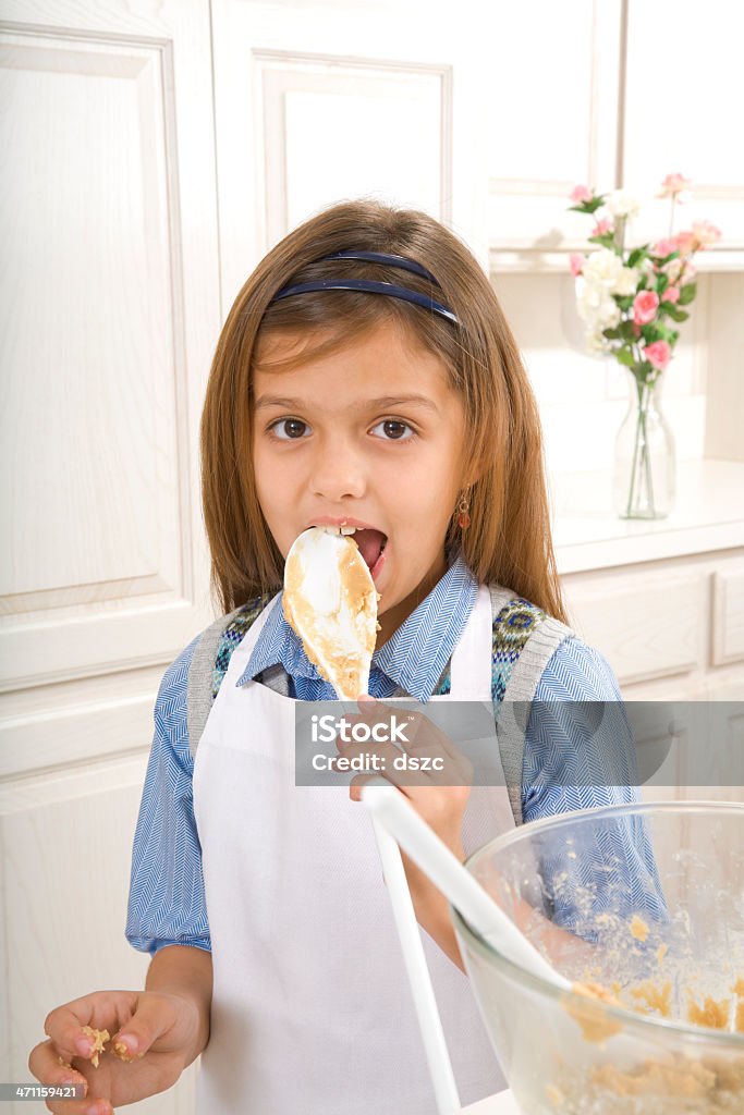 8 años de edad Chica comiendo masa mientras hornear galletas con pedacitos de chocolate - Foto de stock de Lamer libre de derechos