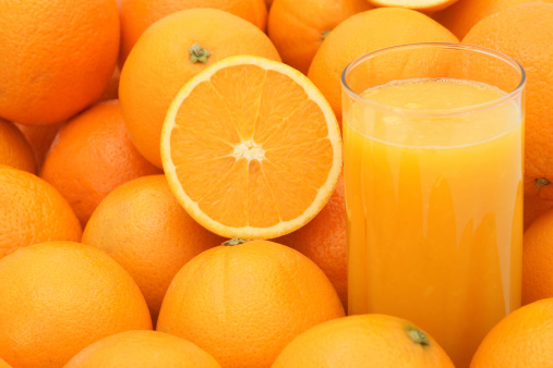 A glass of orange juice next to a group of oranges with a half of orange