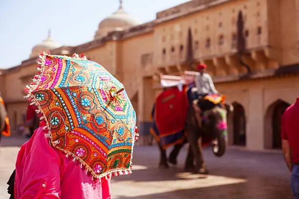 Rear view of woman holding colorful sun umbrella, Amber Fort, Jaipur, India. Indian elephants walking in the background.