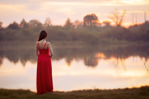Woman in red dress standing near the lake 