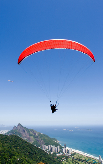 Paraglider flying over forest and Sao Conrado beach. Two Brothers mountains in the background Ipanema right behind them). Rio de Janeiro, Brazil.