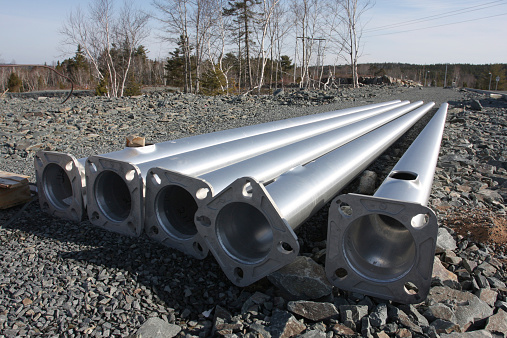 Vertical sections of aluminum lighting standards ready to be erected on a new road construction project.