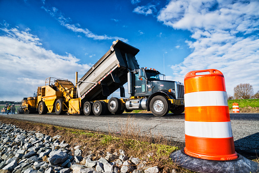 Rising Sun, Maryland USA - April 23, 2015: Allan Myers/American Infrastructure's road resurfacing crew lying a new asphalt layer on the West bound lane of Route 274, about 3 miles outside of town. The asphalt paving machine lays a new layer of hot asphalt down as they work to resurface the road in early Spring, with a traffic drum in the foreground.