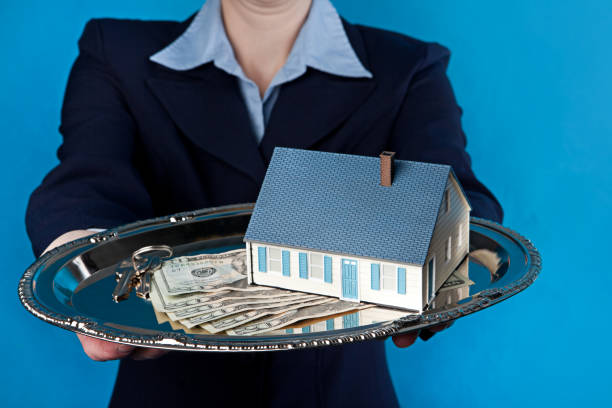 Real Estate On A Silver Platter A woman holding a house with cash and keys on a silver platter. silver platter stock pictures, royalty-free photos & images