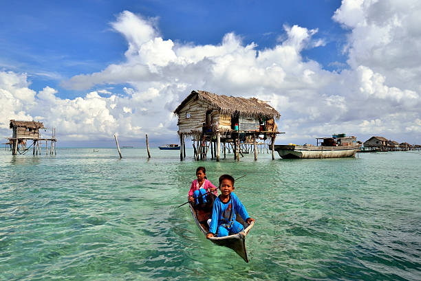 Bajau Sea Gypsies Kids, Bodgaya Island, Sabah Borneo Semporna, Sabah, Malaysia - April 19, 2015: Unidentified Sea Gypsies kids paddle a boat at Sea Gypsy village in Bodgaya Island, Semporna, Sabah, Malaysia. They inhabit villages built on stilts in the middle of ocean. Boat is the main transportation in the area.  mabul island stock pictures, royalty-free photos & images