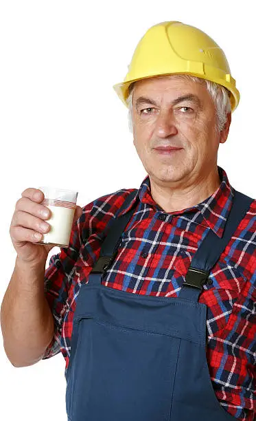 A manual worker in an overall and a helmet holding a glass of milk. Isolated on white.