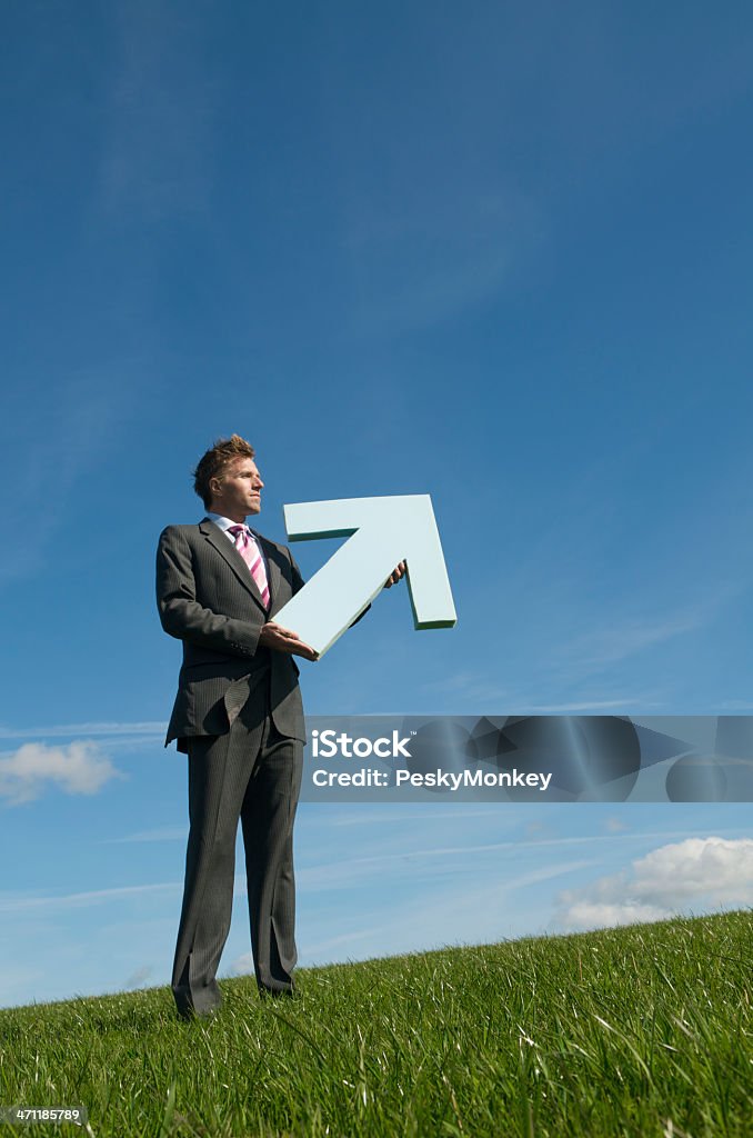 Businessman Holding Big Arrow Pointing Up Blue Sky Green Meadow Businessman holding a big arrow pointing up into blue sky on the slope of a green meadow 30-39 Years Stock Photo