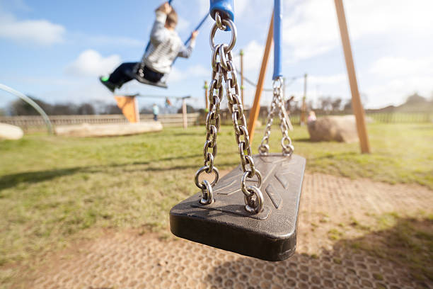 Empty playground swing Empty playground swing with children playing in the background concept for child protection, abduction or loneliness swing play equipment photos stock pictures, royalty-free photos & images