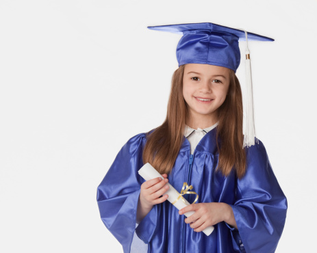 Little kindergartner wearing her cap and gown, holding her diploma that says she's ready for the