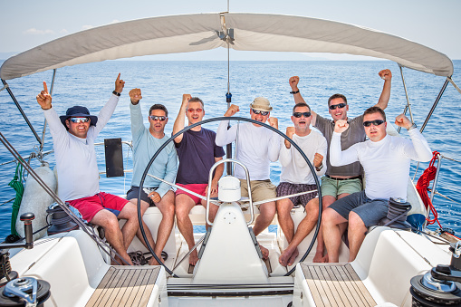 Happy sailing crew of seven sailors on sailboat.