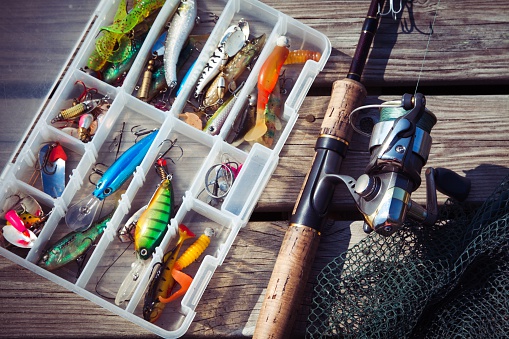 Fishing Lures in tackle boxes with spinning rod and net on wooden pier