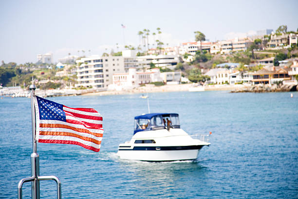 The flag of the United States flutters in the wind on a stainless steel flagpole at the stern of a motor yacht. Marina in the port city in beautiful summer sunny weather.