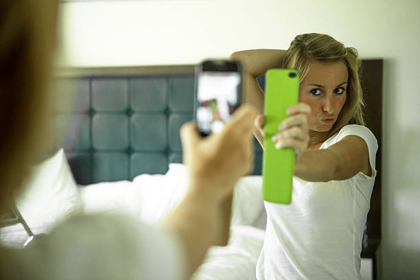 Young woman taking selfie showing off-Bedroom Young woman in an hotel room taking a selfie in the morning, sunlight coming in the room. She is taking a self portrait from the reflection in the mirror using her mobile phone. fish lips stock pictures, royalty-free photos & images