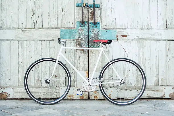 Photo of White bike leaning against dingy wooden gate doors