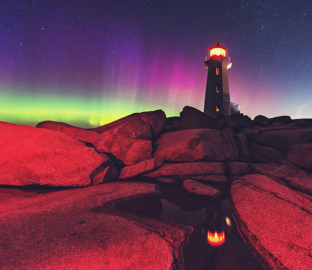 The Aurora Borealis paints the Northern skies with colour at Peggy's Cove Lighthouse. Long exposure with a photographer's headlamp providing the red lighting to the foreground.