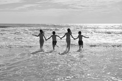 Black and white photo. Female kisses and hugs male standing barefoot on water with big waves ocean and enjoying a summer day. Man hugging woman on beach sea. Couple in love kissing on seashore.