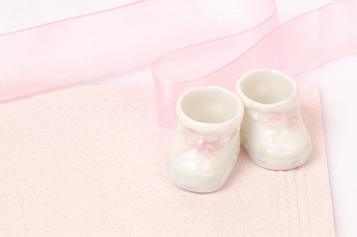 Little baby booties and pink ribbon on embossed pink paper, high key