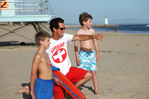 Male lifeguard at the ocean beach with two young children.