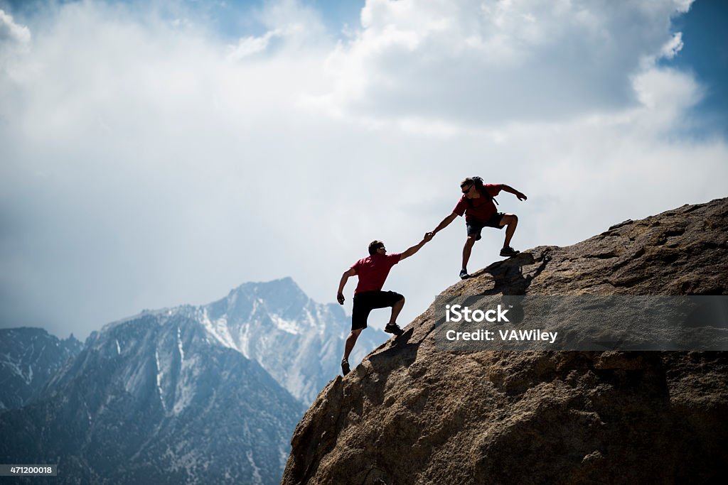 Helping hikers One climber helping another to the summit of a giant boulder  Mountain Stock Photo