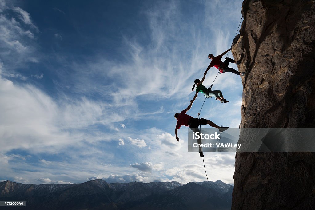 extreme rappelling Three rock climbers helping one from falling in a dramatic setting  Teamwork Stock Photo