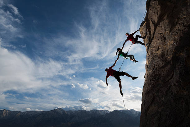 extreme rappelling Three rock climbers helping one from falling in a dramatic setting  mountaineering stock pictures, royalty-free photos & images