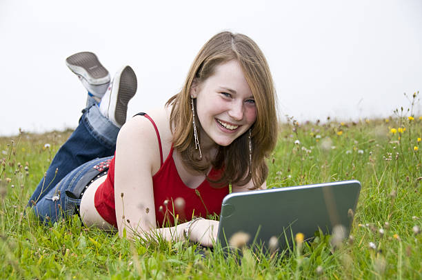 подросток mit ноутбук auf der wiese liegen in kamera lachen - carl jung стоковые фото и изображения