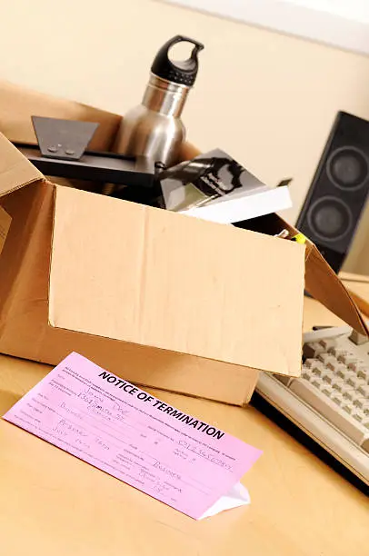 A "pink slip" (notice of termination) lies next to a cardboard box on an office desk where the terminated employee has been packing up his belongings. Shot at Toronto Echucalypse 2009.