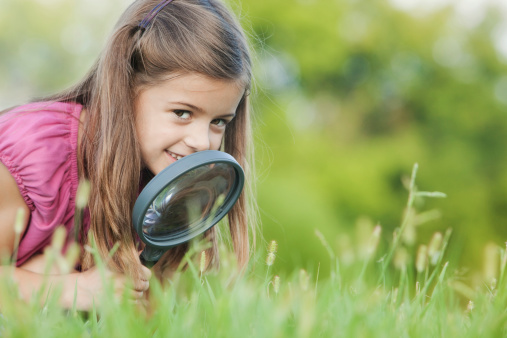 Little girl smiling as she looks up from her magnifying glass.  She was hunting for ladybugs.