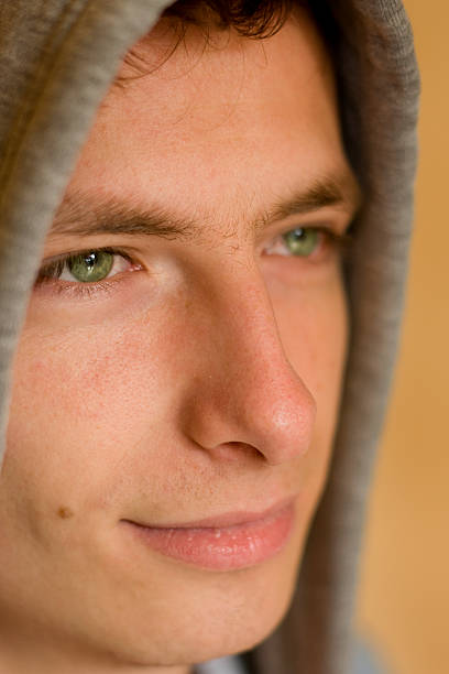 Close up face of an young man is looking to the camera,  in the street. Man with calm emotions on his face looks into the camera - outdoors. Handsome guy posing outdoors on green trees background.