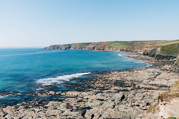 Landscape of coastline leading west towards Porth Sulinces near Porthleven in Cornwall, south-west England. Cliffs lead to a rocky shoreline and the sea below. It is a beautiful sunny day in summer with calm blue sea.